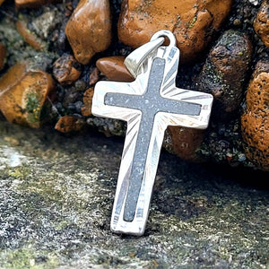 Sterling silver cross pendant with grey stone inlay on a mossy rock surface. Religious jewelry, handcrafted.
