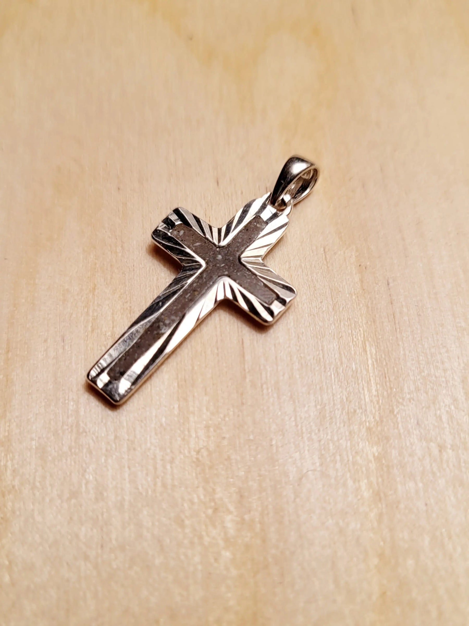 Sterling silver cross pendant for ashes on wood surface. Memorial jewelry shows a .925 cross necklace close up.
