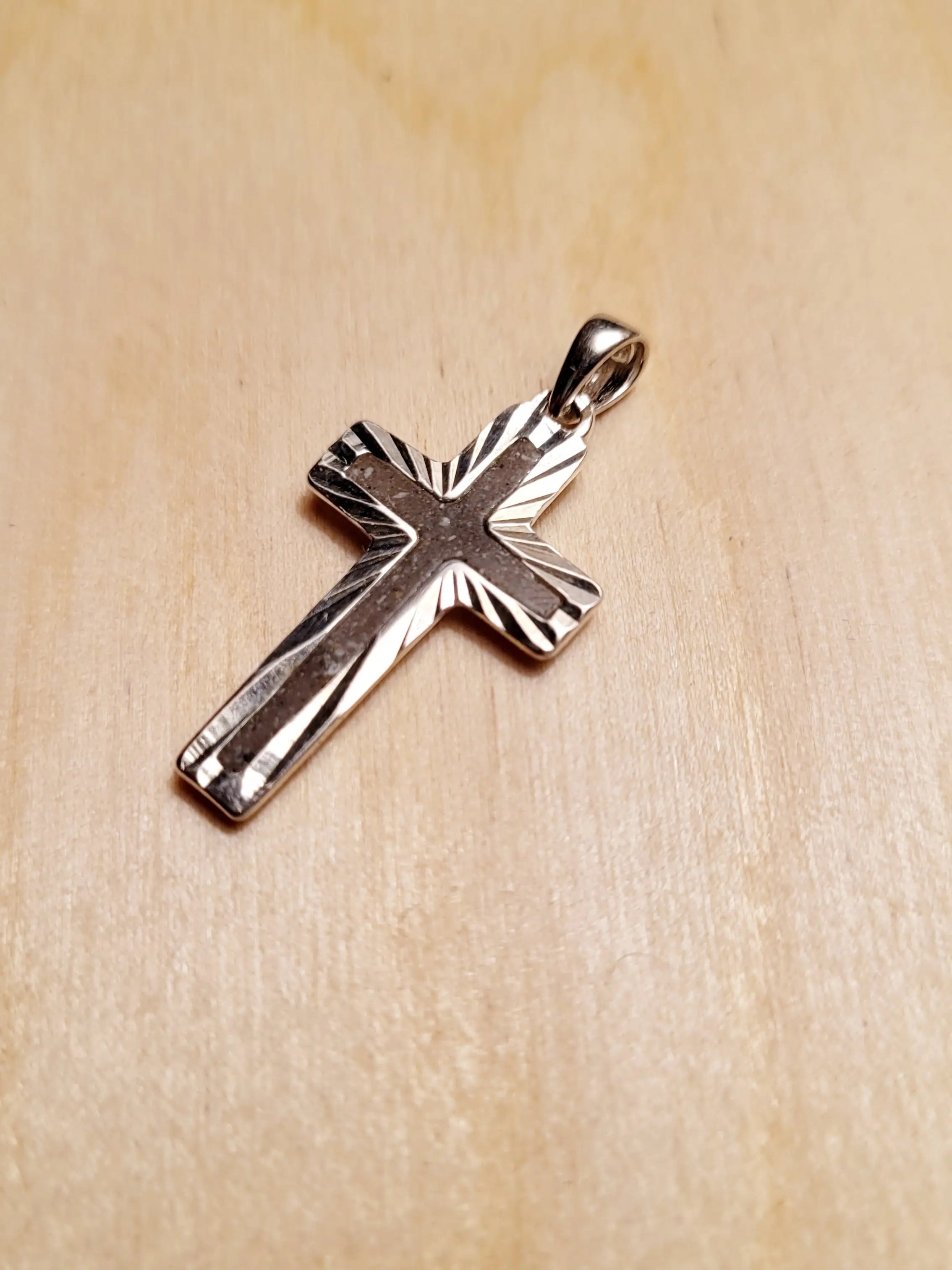 Sterling silver cross pendant for ashes on wood surface. Memorial jewelry shows a .925 cross necklace close up.