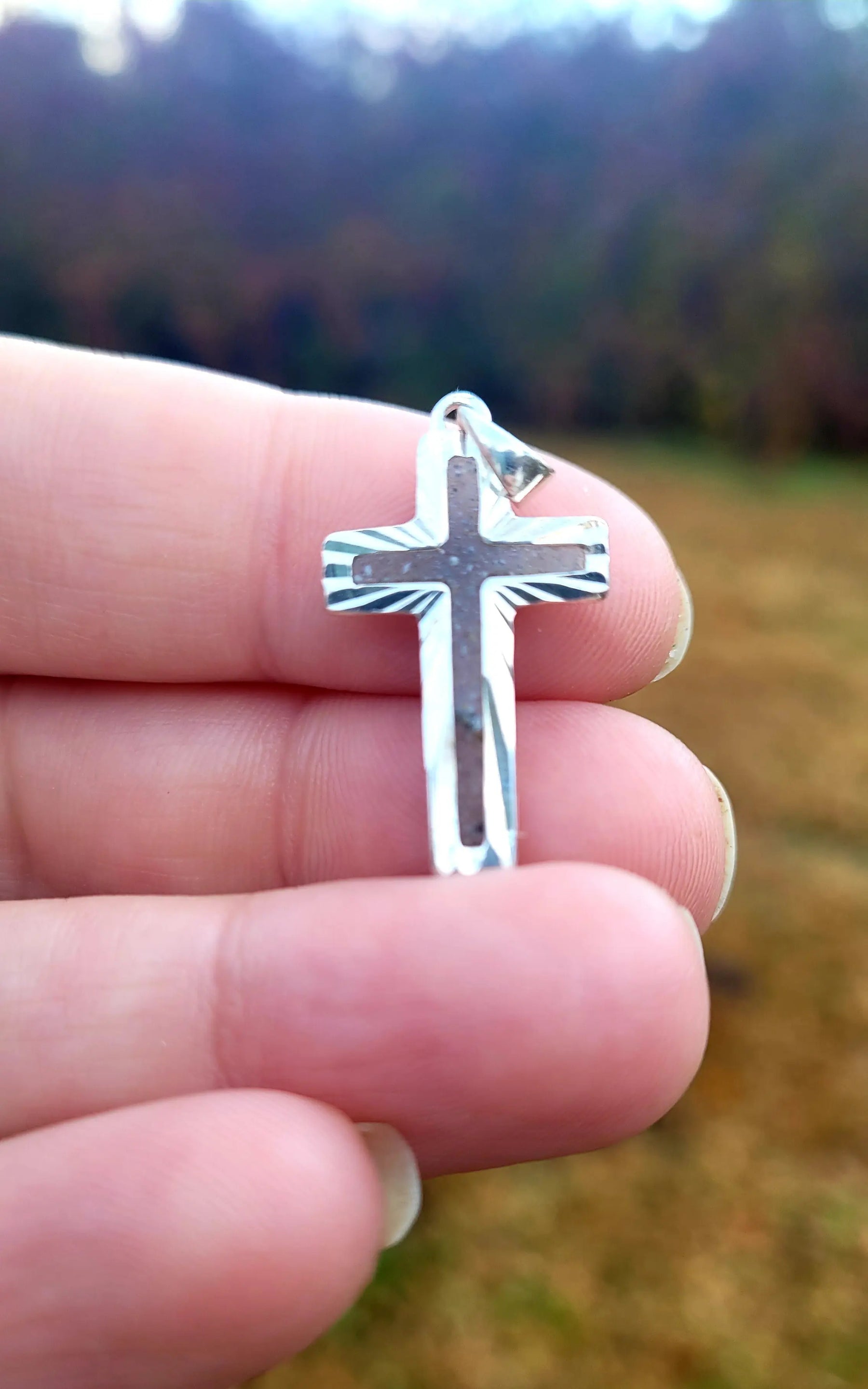 Sterling Silver Cross Pendant: .925 silver Christian jewelry held in hand with blurred outdoor background.