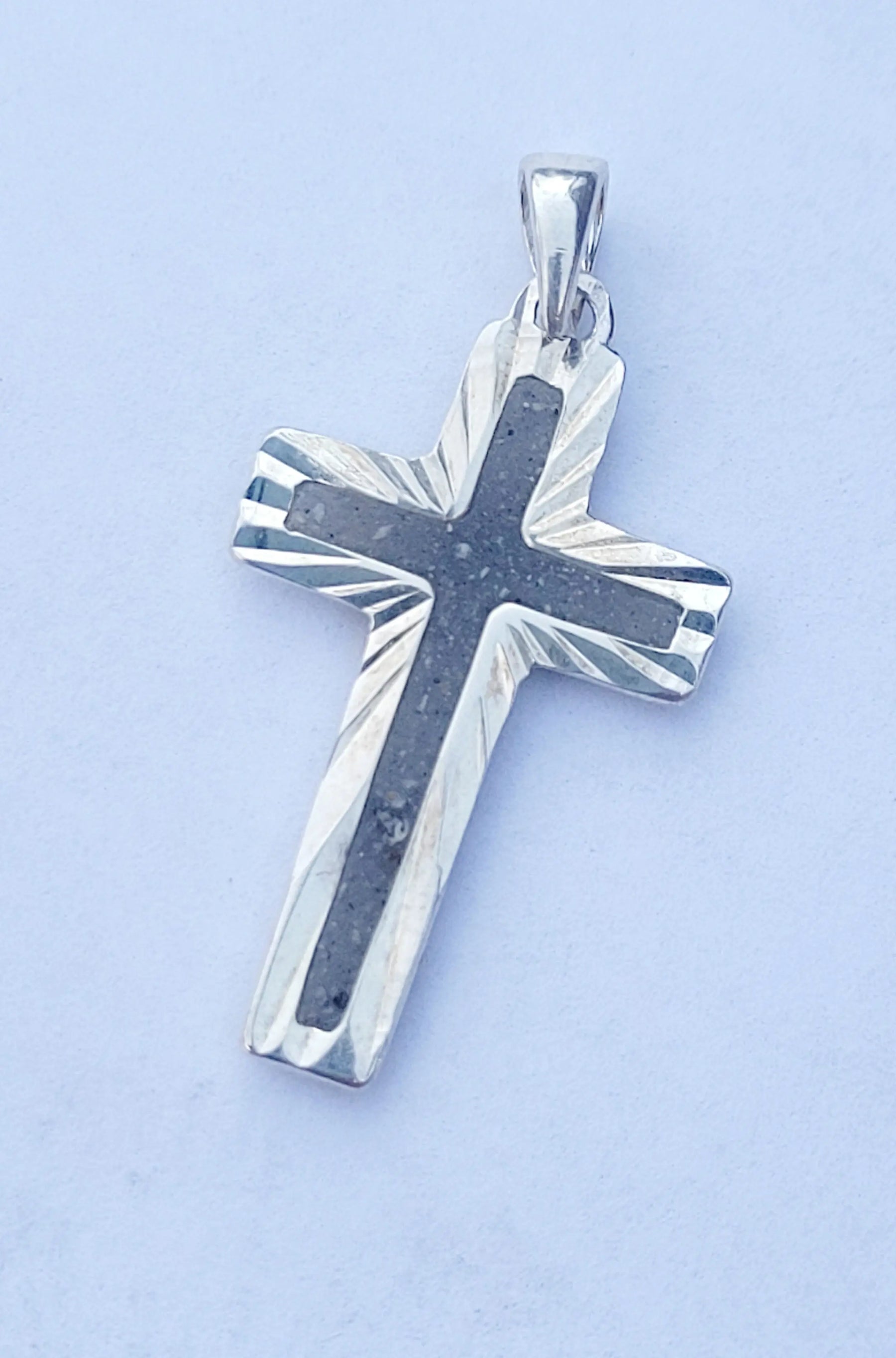 Sterling silver cross pendant with dark stone inlay, viewed close-up on a white background.