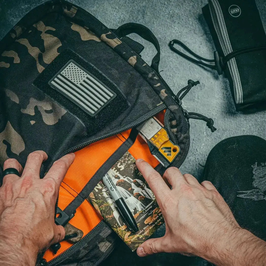 Camouflage backpack with American flag patch, opening to reveal contents.