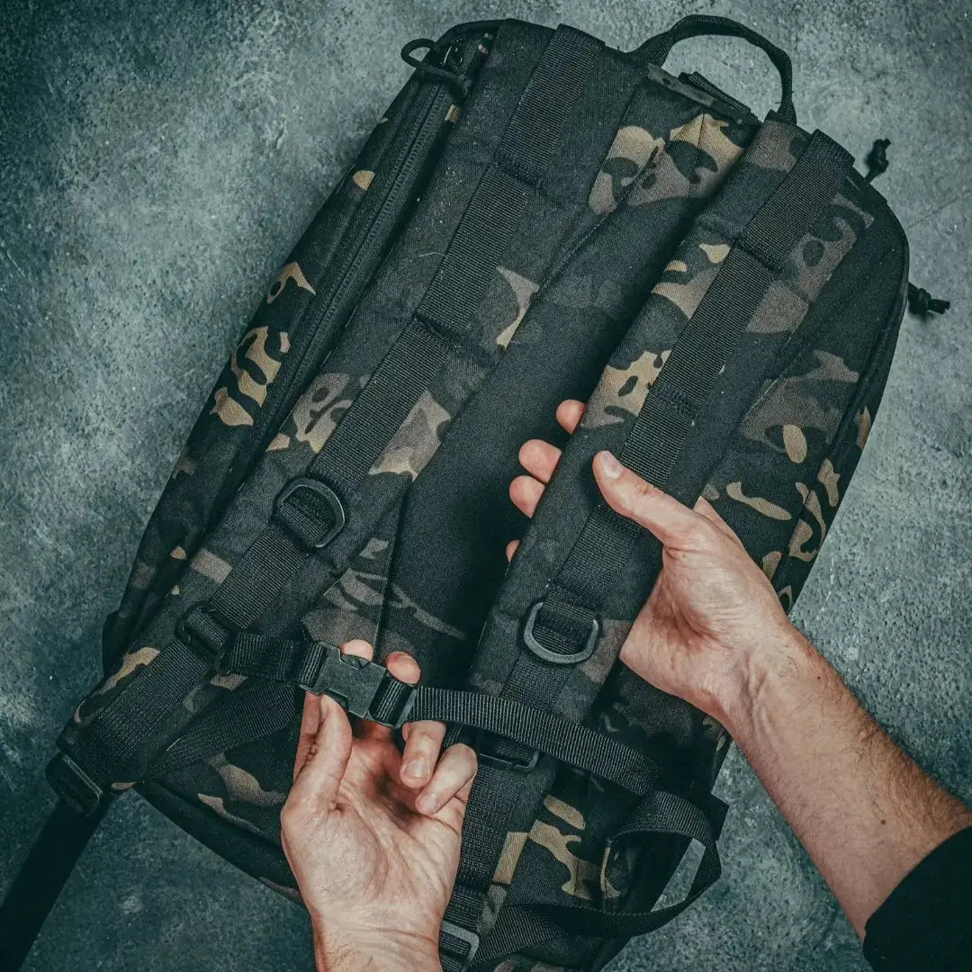 Hands adjusting buckle strap on black camouflage 24 Hour backpack