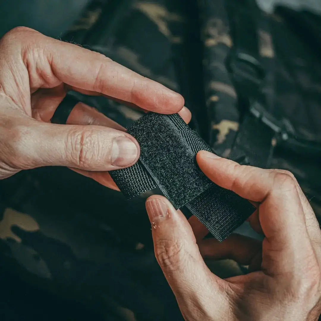 Hands attaching black velcro strap to a 24 HOUR BACKPACK 500D.