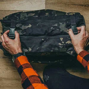 Black and green camouflage backpack with black buckles being adjusted by hands.
