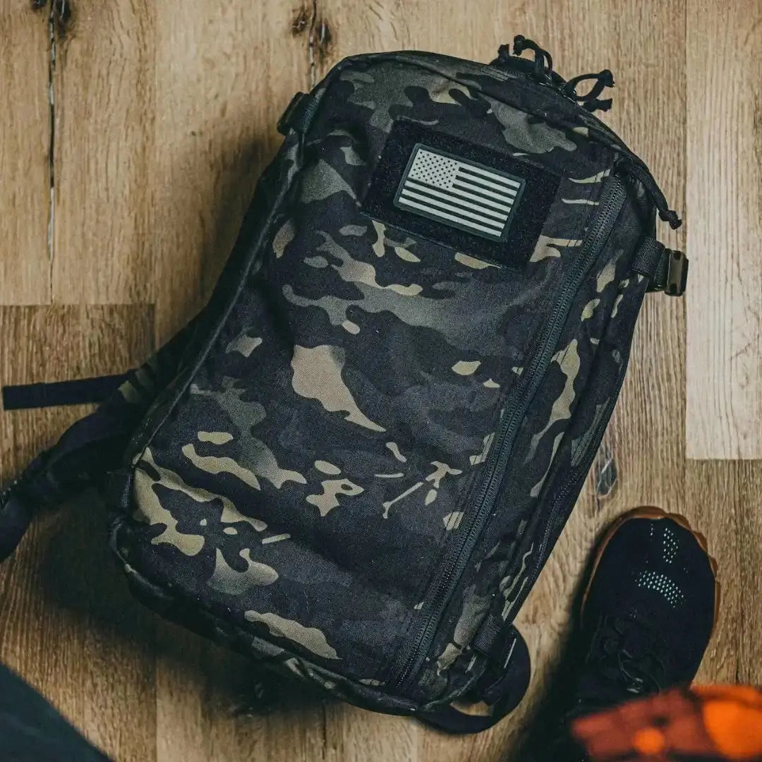Camouflage backpack with American flag patch and shoe on wooden floor.
