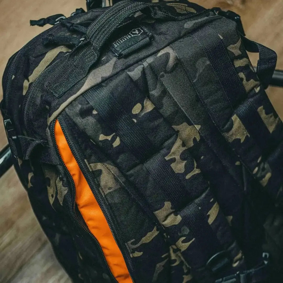 Black and tan camouflage backpack with orange interior zipper detail.
