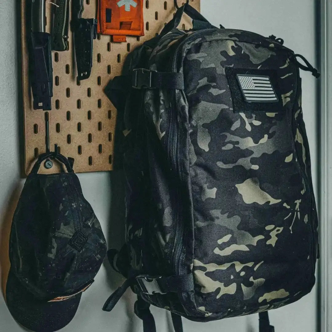 24 Hour Plus Backpack in camouflage pattern with US flag patch displayed on wall.