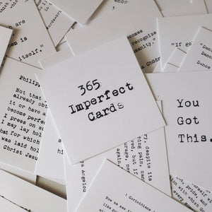 Pile of white cards with black typewriter text, featuring "365 Imperfect Cards".