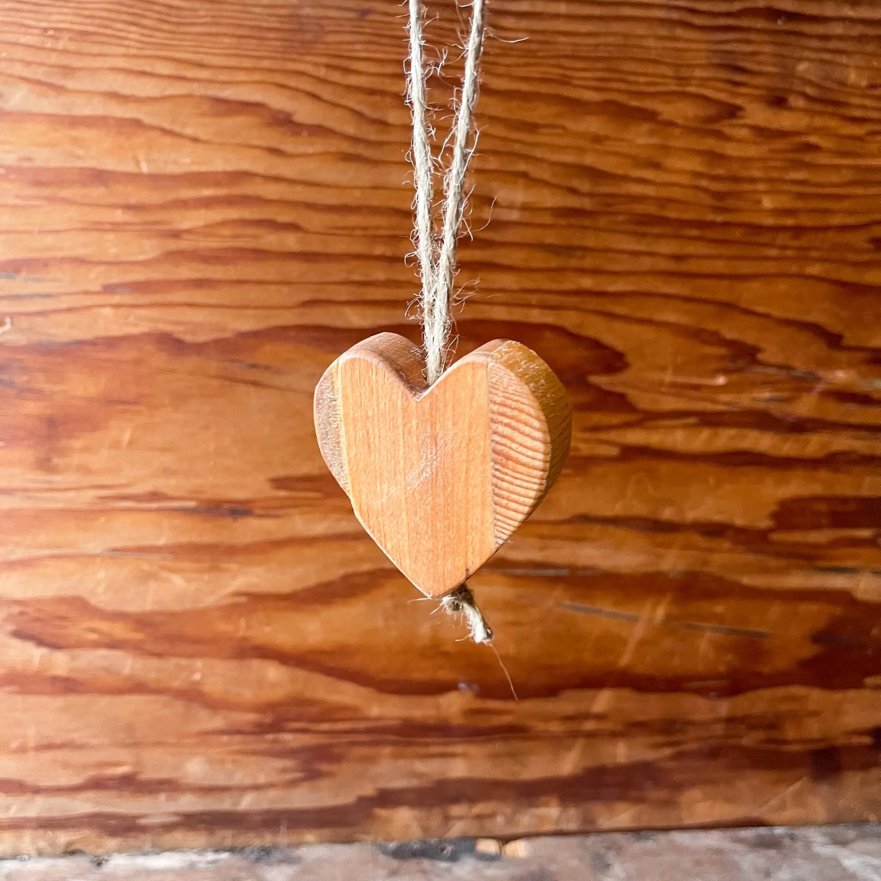 Wooden heart ornament with natural jute twine hanging against a wooden background.
