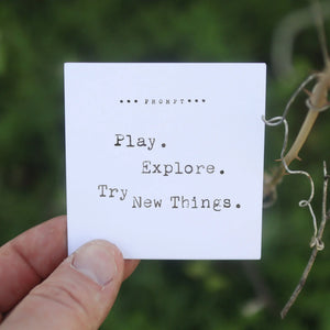 365 Imperfect Cards prompt "Play. Explore. Try New Things." held by a hand