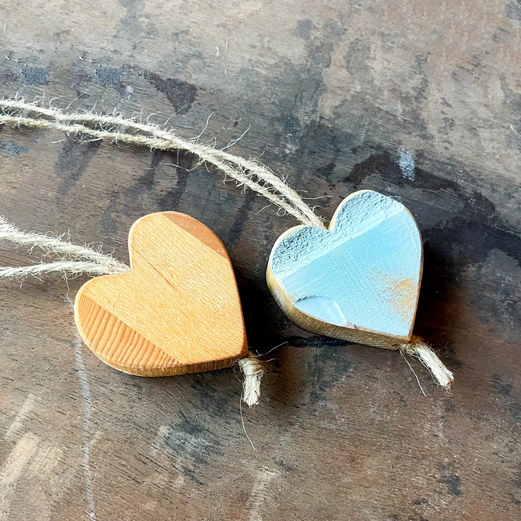 Two wooden heart ornaments on twine, one natural wood, one light blue painted.