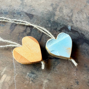 Two wooden heart ornaments on twine, one natural wood, one light blue painted.