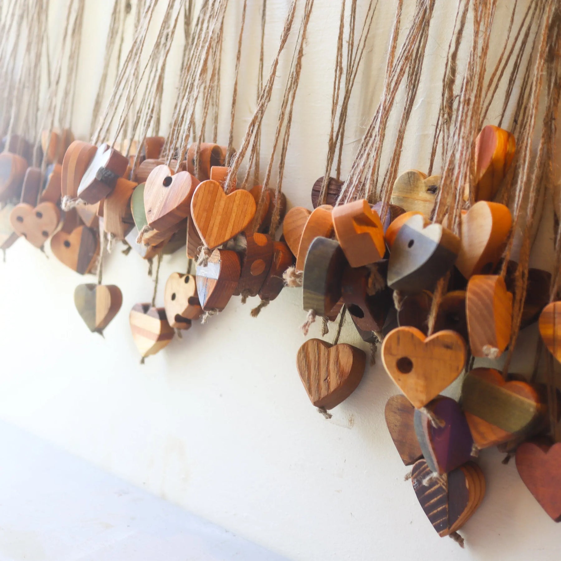 Wooden heart ornaments with jute twine hanging against a white wall.