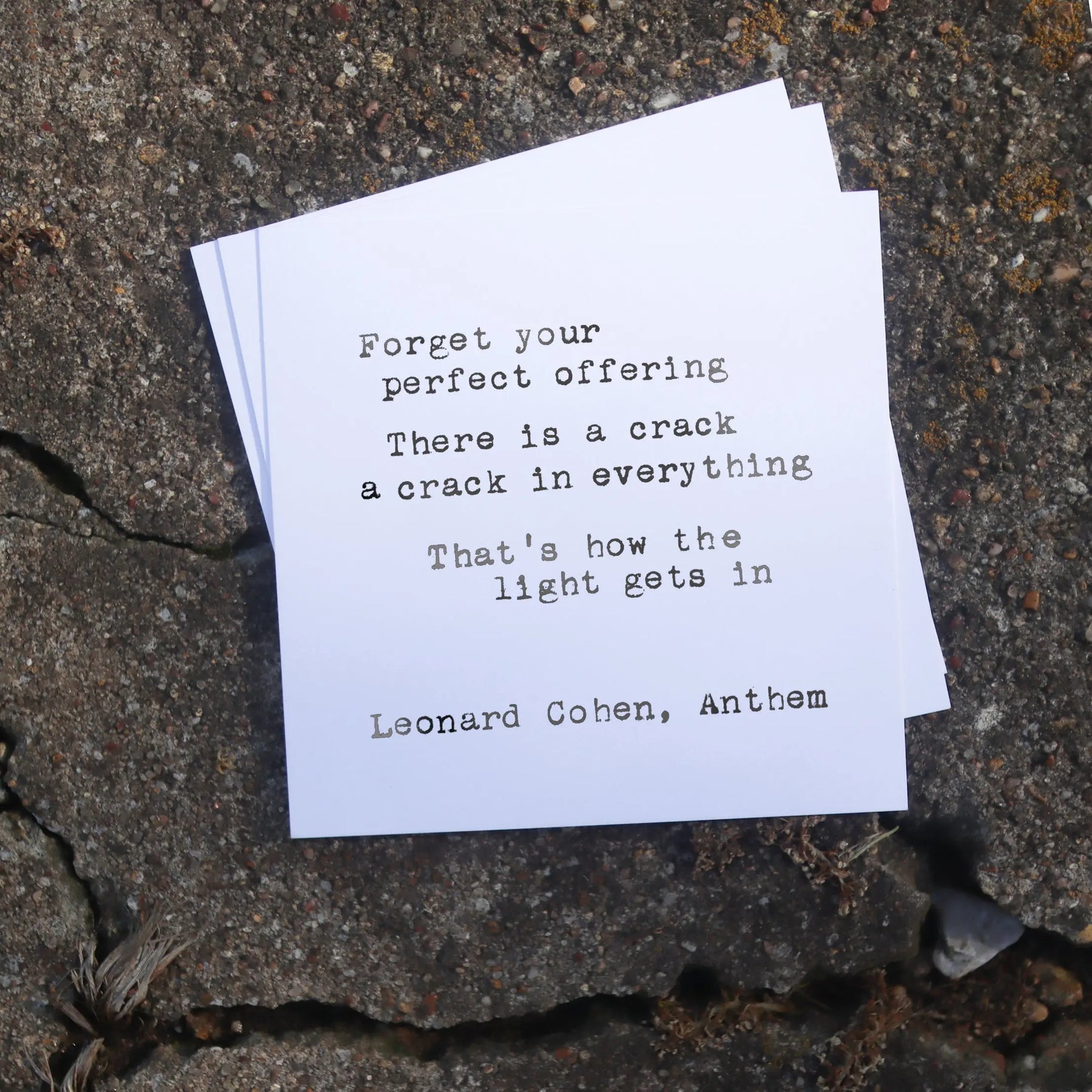 Quote by Leonard Cohen on a white card placed on a concrete surface.