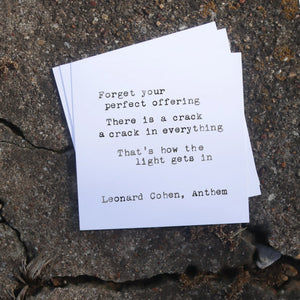 Quote by Leonard Cohen on a white card placed on a concrete surface.