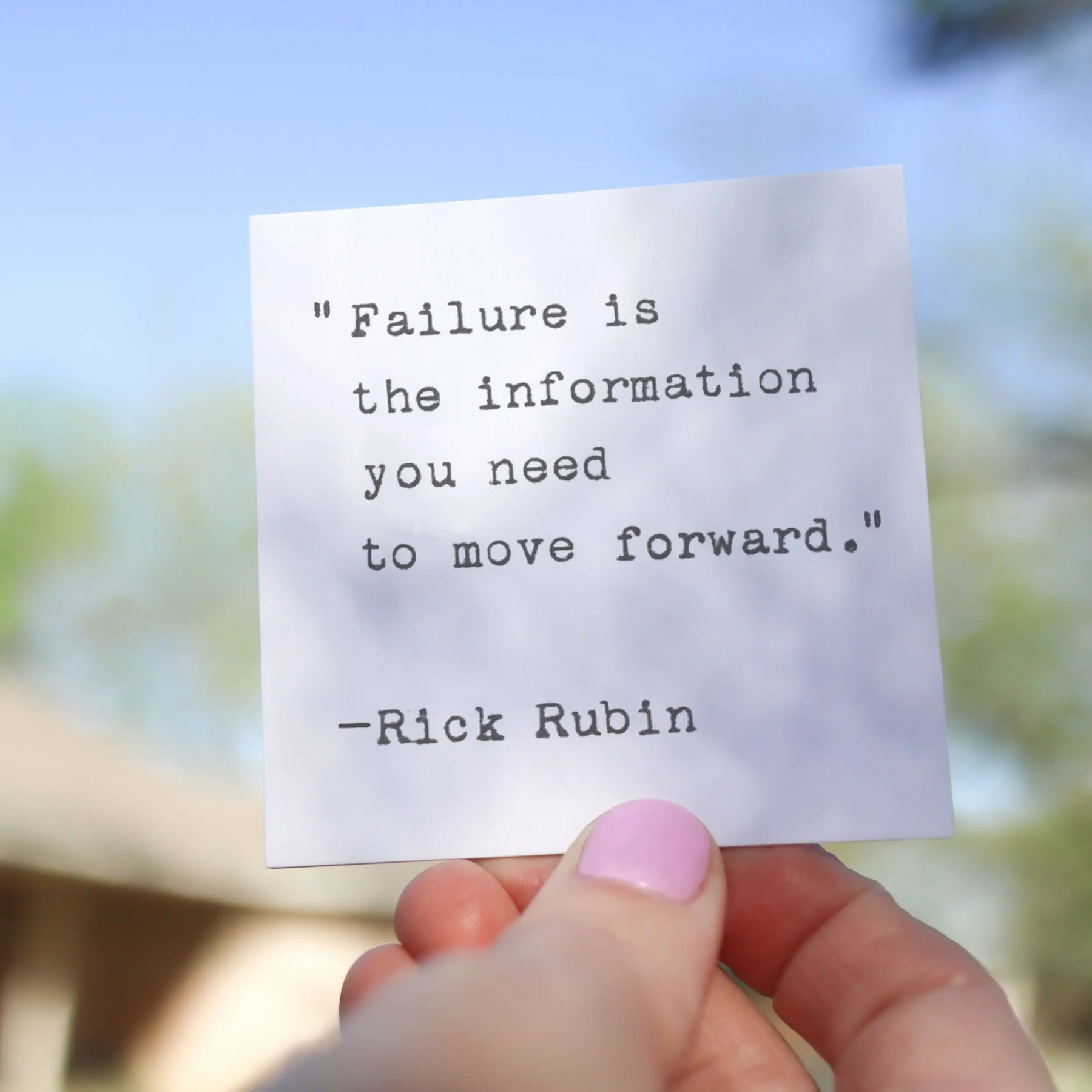A hand holds a white card with a quote typed on it.