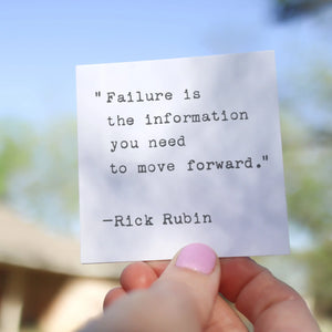 A hand holds a white card with a quote typed on it.