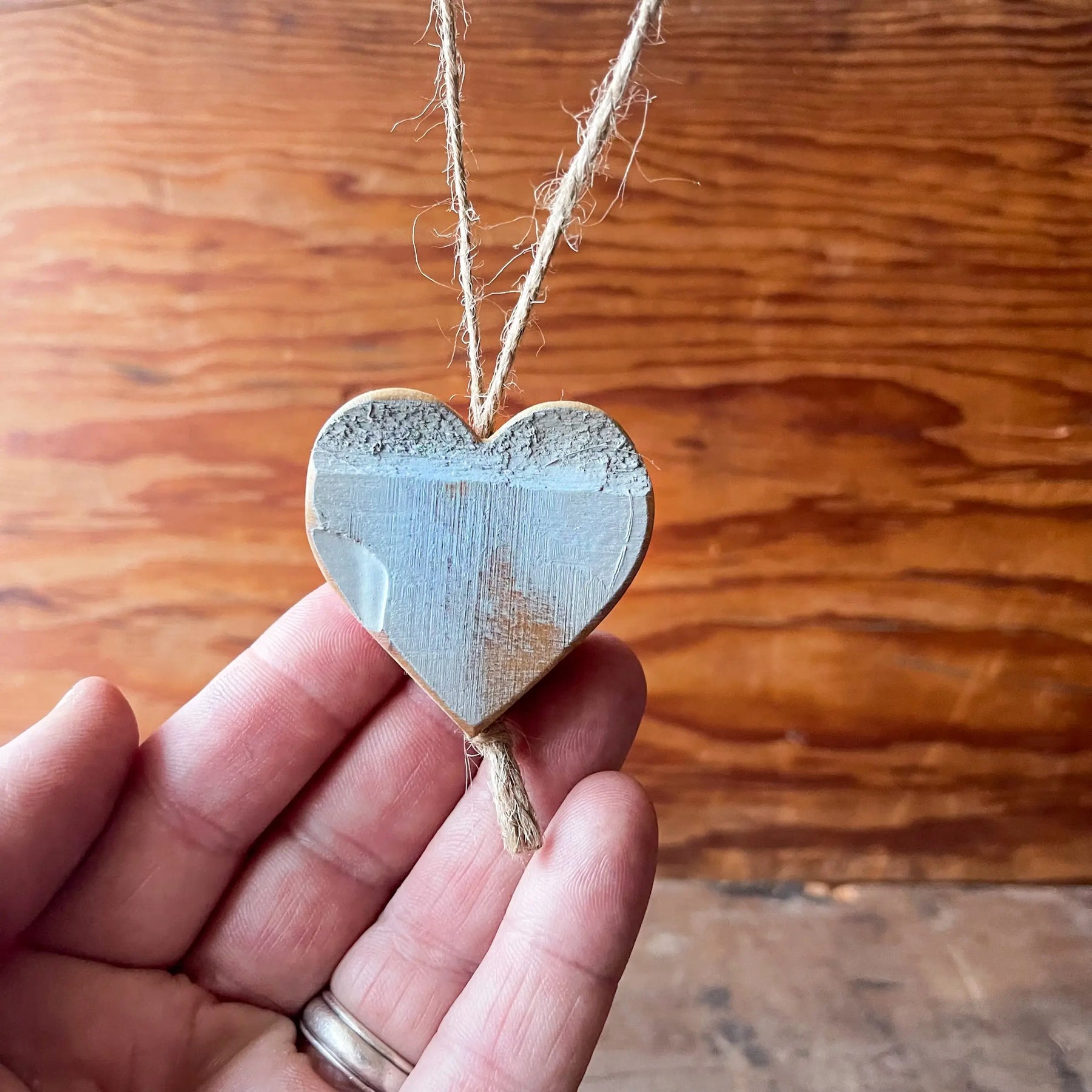Wooden heart charm with twine hanging and a hand holding it.