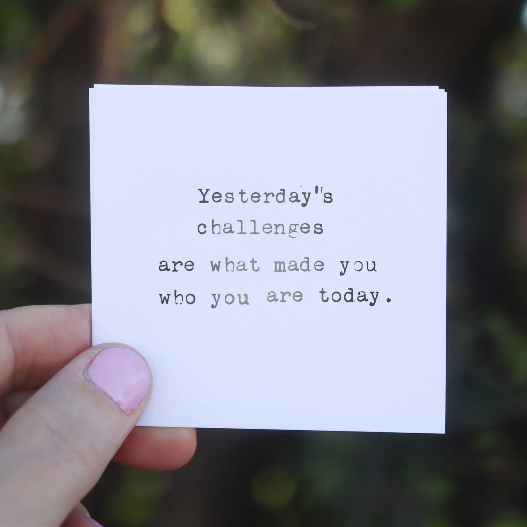 A hand holds a white card with a quote typed in gray ink.