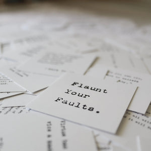 Card with "Flaunt Your Faults" in typewriter font among scattered papers.