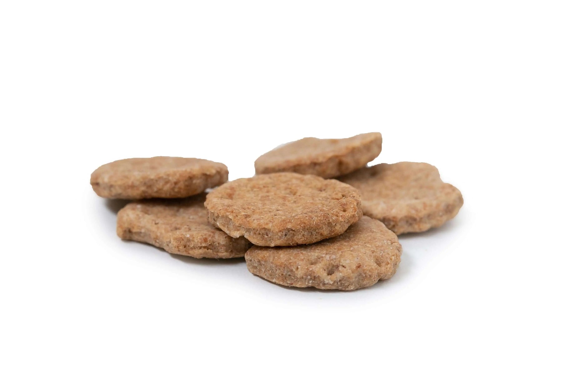 Pile of round, textured, brown dog biscuits on a white background.
