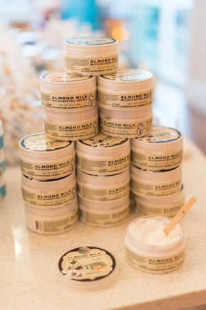 Jars of Almond Milk Wildcrafted Arnica Herbal Salve stacked with one open jar and spatula.