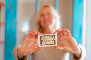 Woman holding a bar of Almond Milk Soap with a floral and bee label.