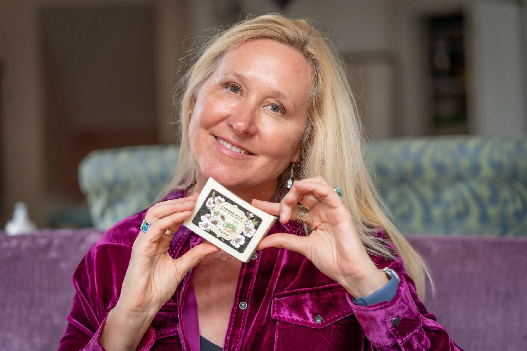 Woman holding a bar of Almond Milk Soap with floral packaging.