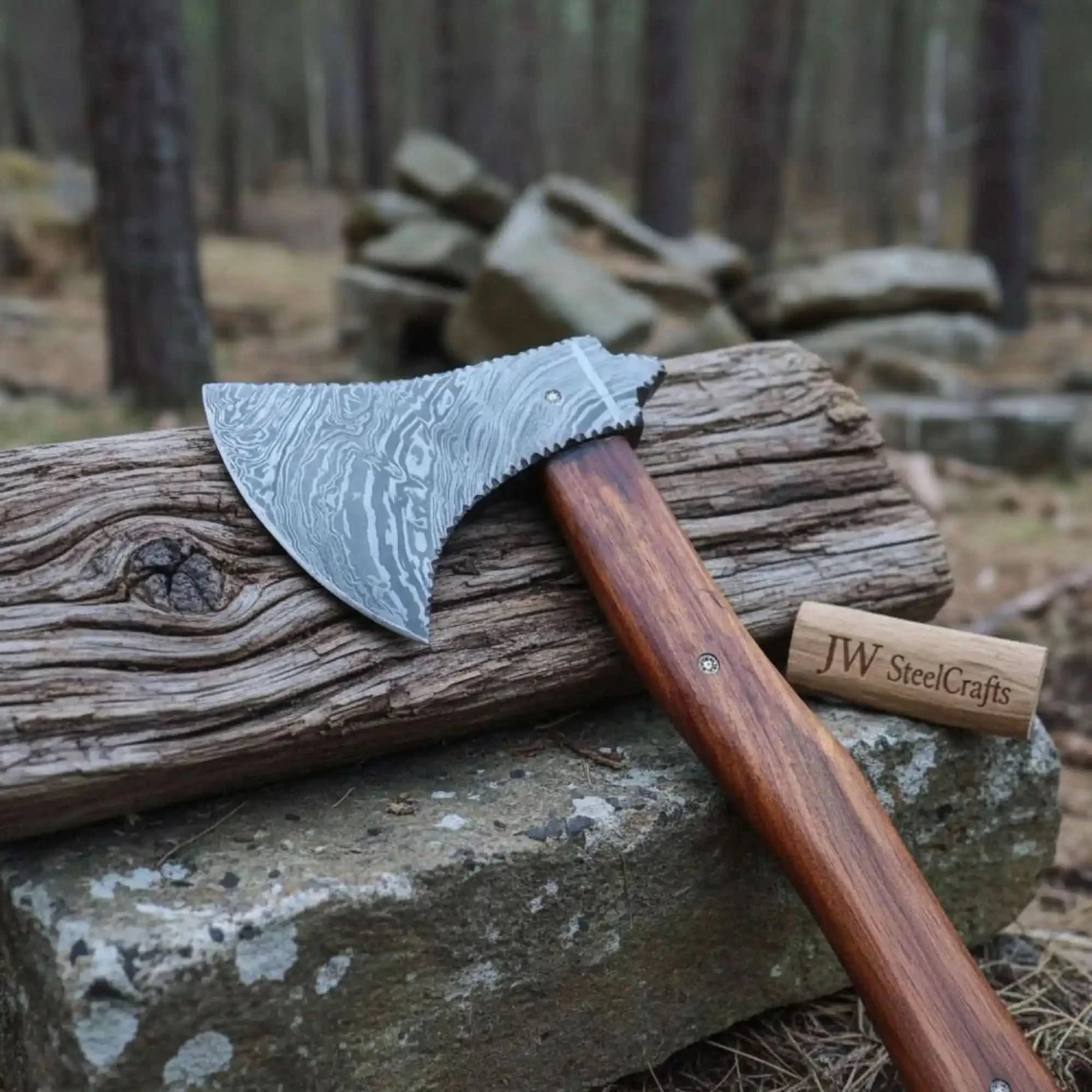Damascus steel axe head with premium handle on rustic wood surface