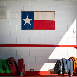 Texas flag made from repurposed fire hose hanging on a white brick wall.