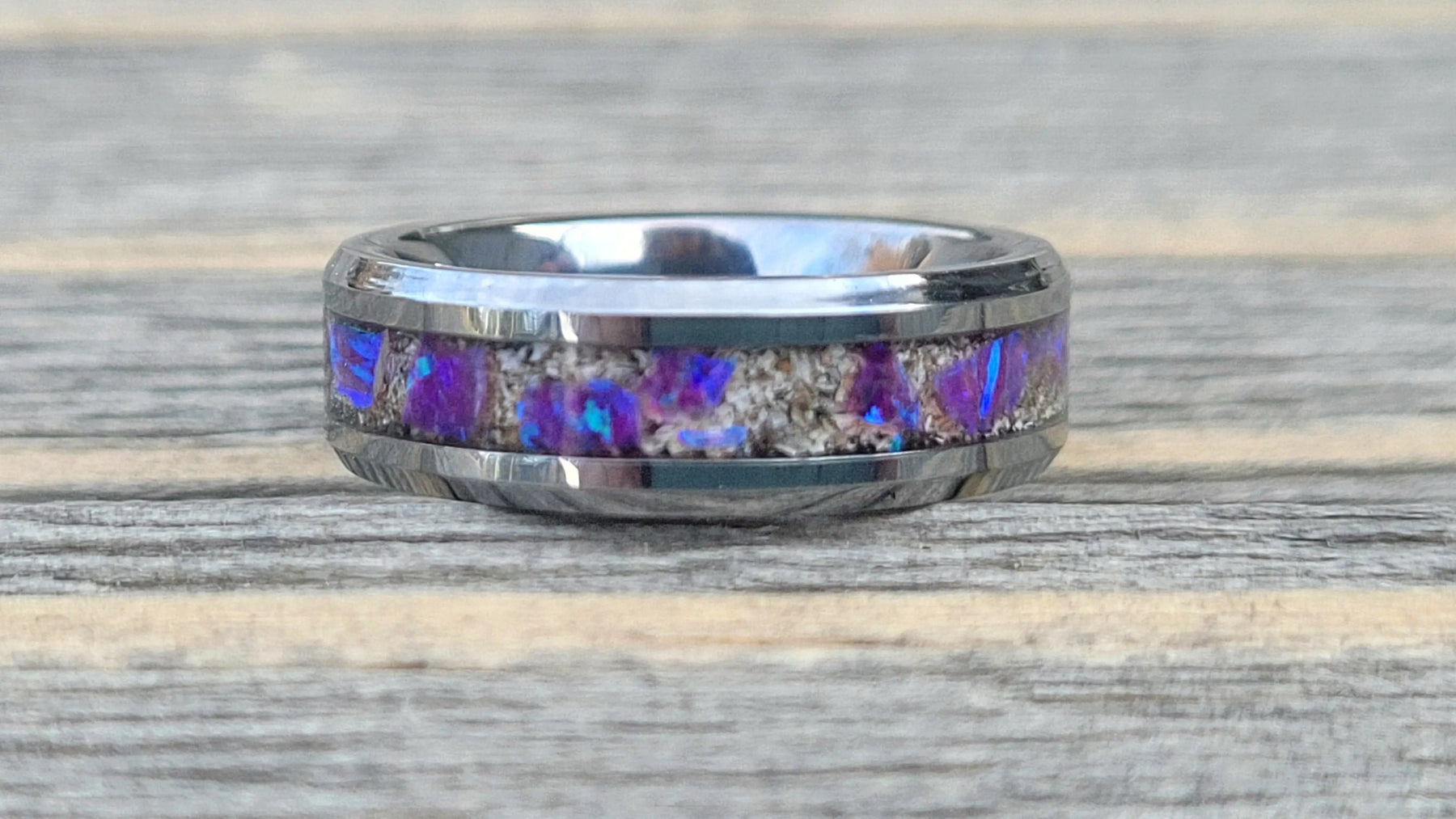Silver memorial ring with amethyst opal and cremation ashes inlay on a wood surface. Close up view.