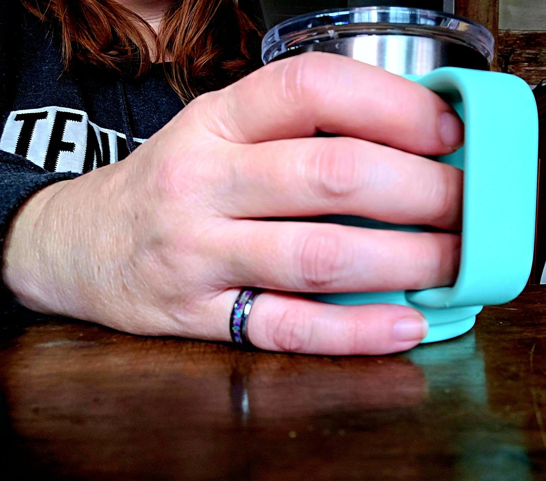 Hand holds turquoise mug, featuring Main Street Collective amethyst opal and ashes ring.