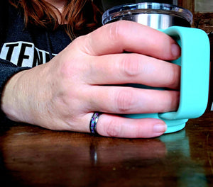 Hand holds turquoise mug, featuring Main Street Collective amethyst opal and ashes ring.