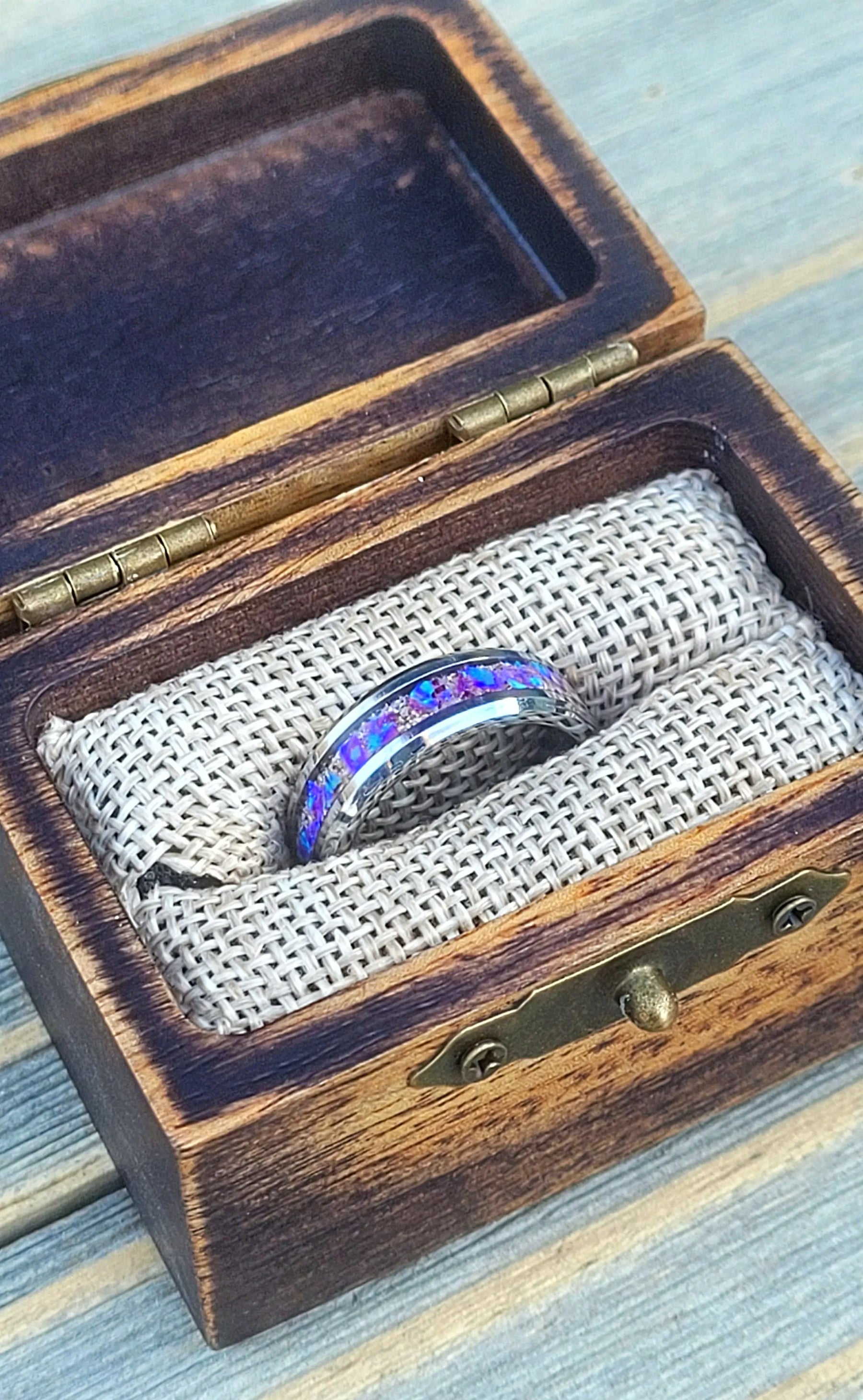 Amethyst opal ring inside a rustic wooden box with metal hinges and a burlap lining.
