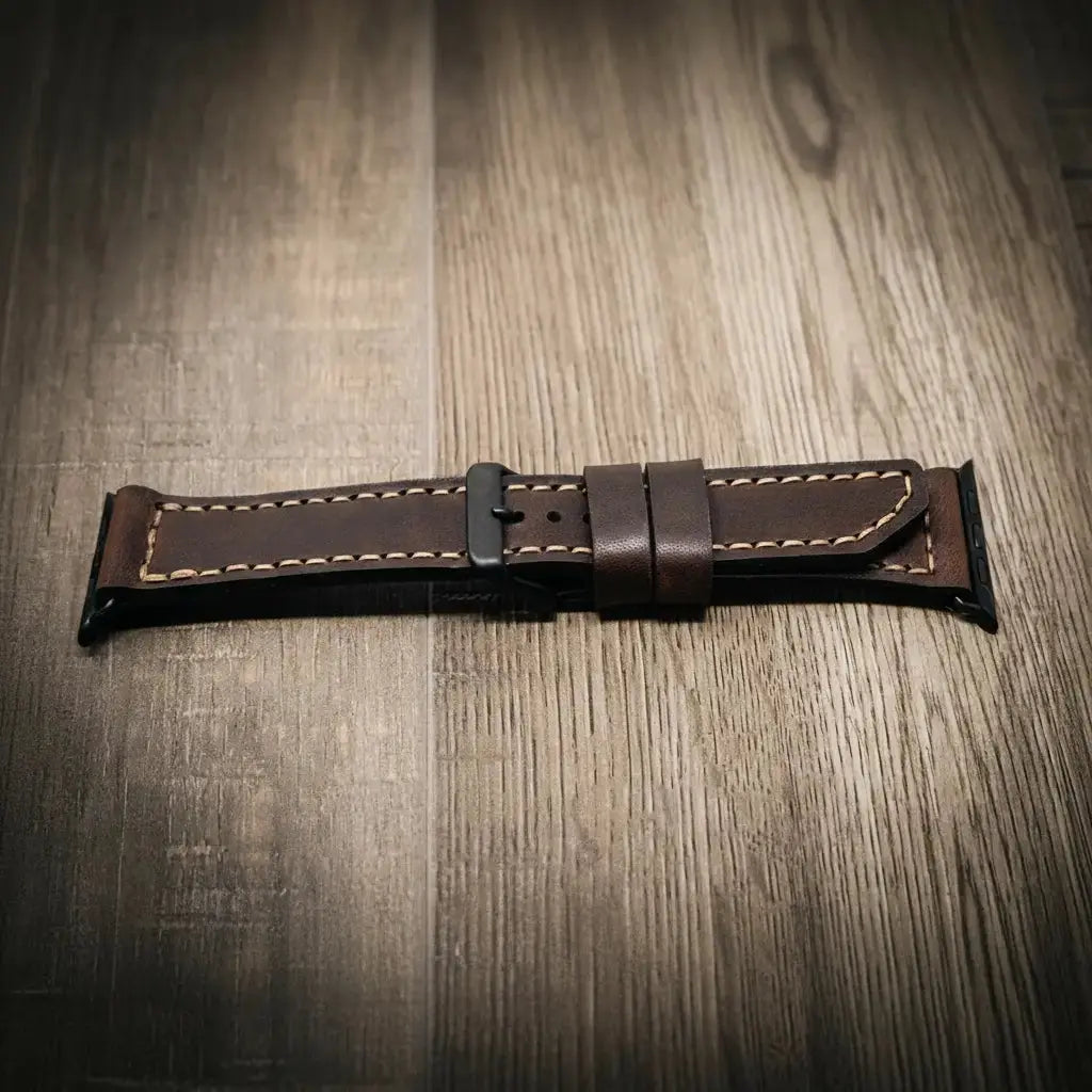 Brown leather Apple Watch band with stitching and a black buckle on a wooden surface.