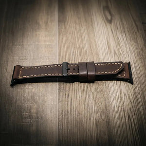 Brown leather Apple Watch band with stitching and a black buckle on a wooden surface.