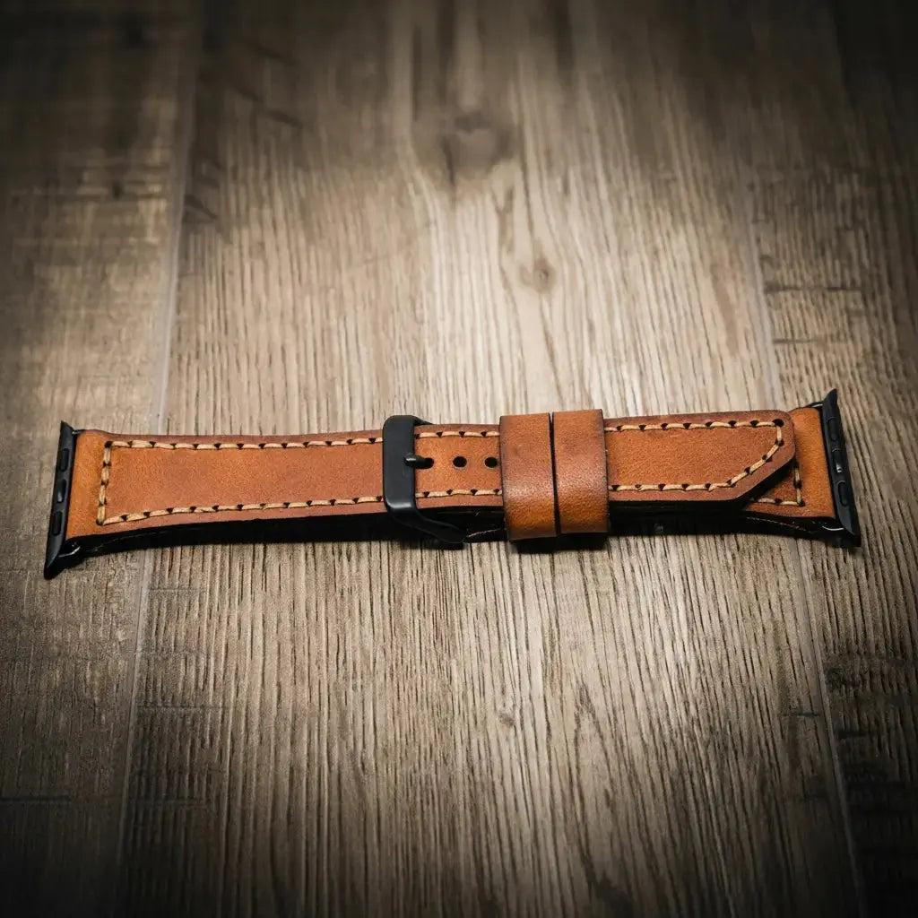 Brown leather Apple Watch band with a black buckle on a wooden background.