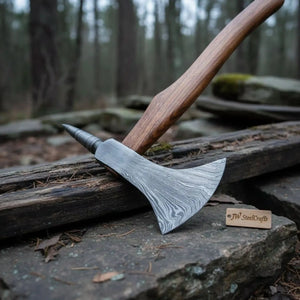 Damascus steel axe head with premium handle on rustic wood surface