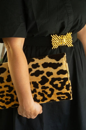 Woman in black dress with leopard print clutch and gold belt buckle.