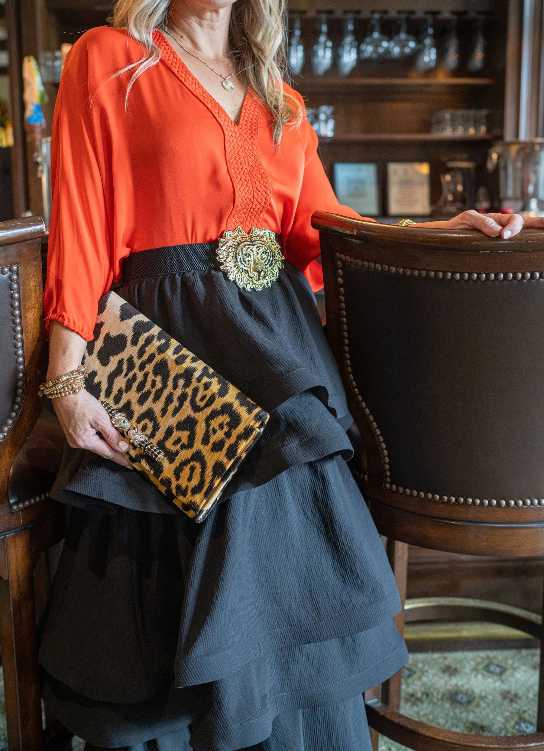 Woman holding a leopard print velvet clutch with a lion head buckle.