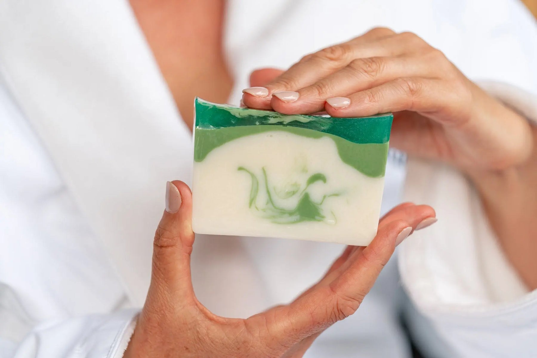Hands holding a handmade balsam and goat's milk soap slice with green and white swirls.