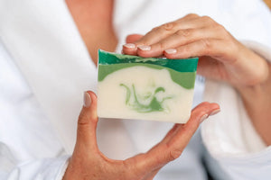 Hands holding a handmade balsam and goat's milk soap slice with green and white swirls.