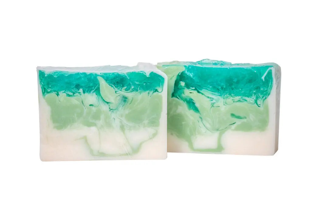 Two bars of handmade goats milk soap with green and white marbled swirls.