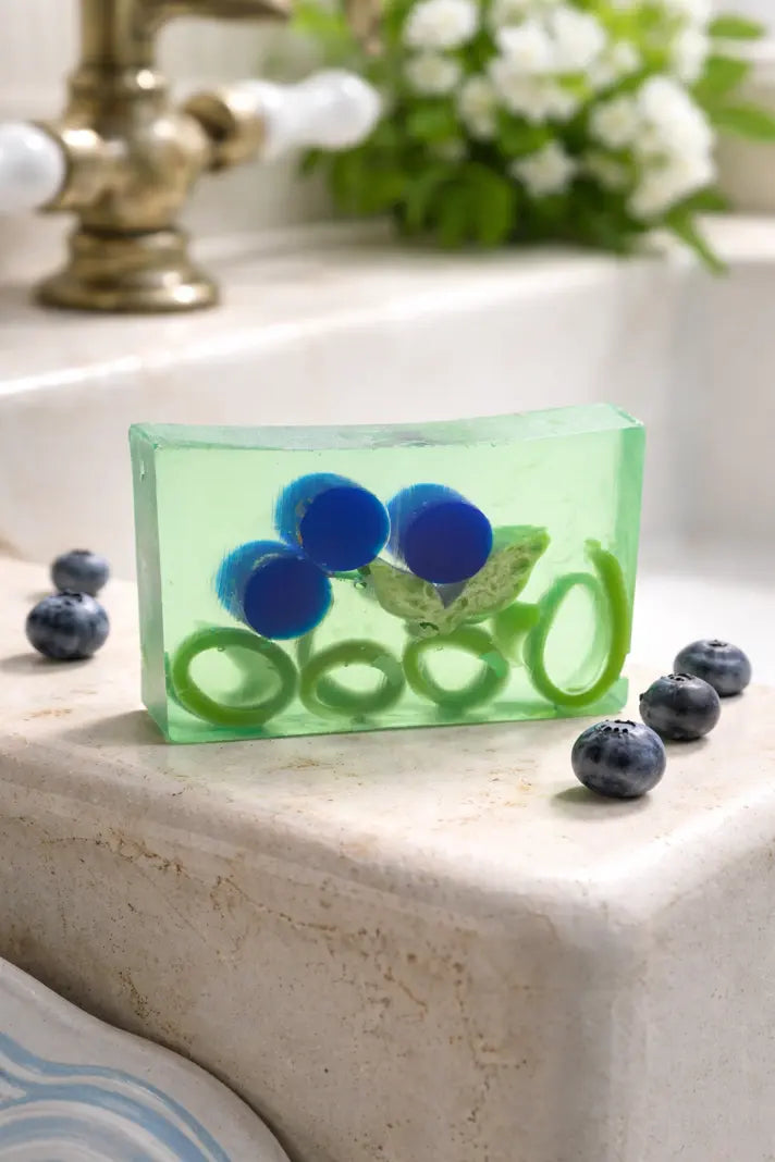 Clear green bar soap with blueberry and green ring inclusions on a stone counter.