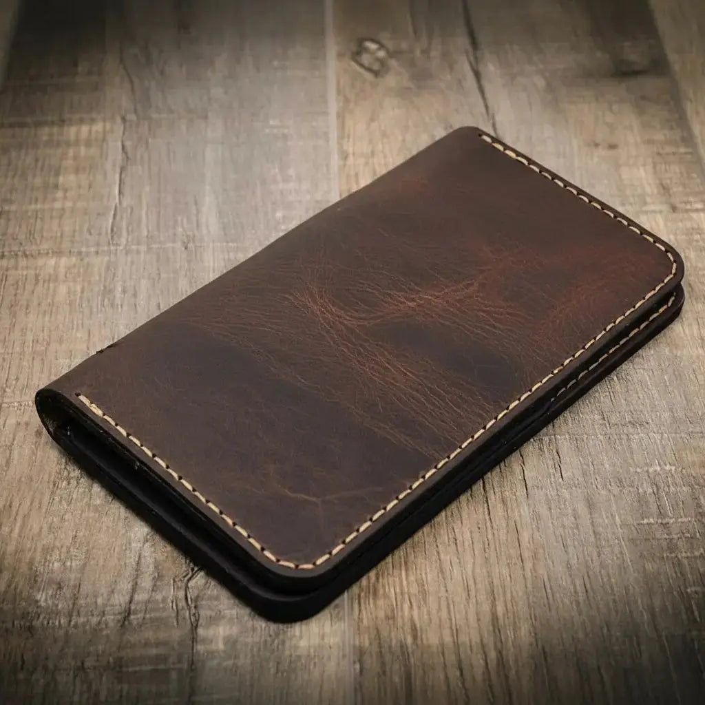 Brown leather long wallet with stitched edges on a wooden surface.