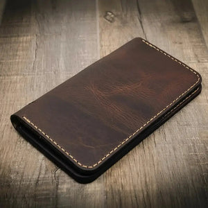 Brown leather long wallet with stitched edges on a wooden surface.