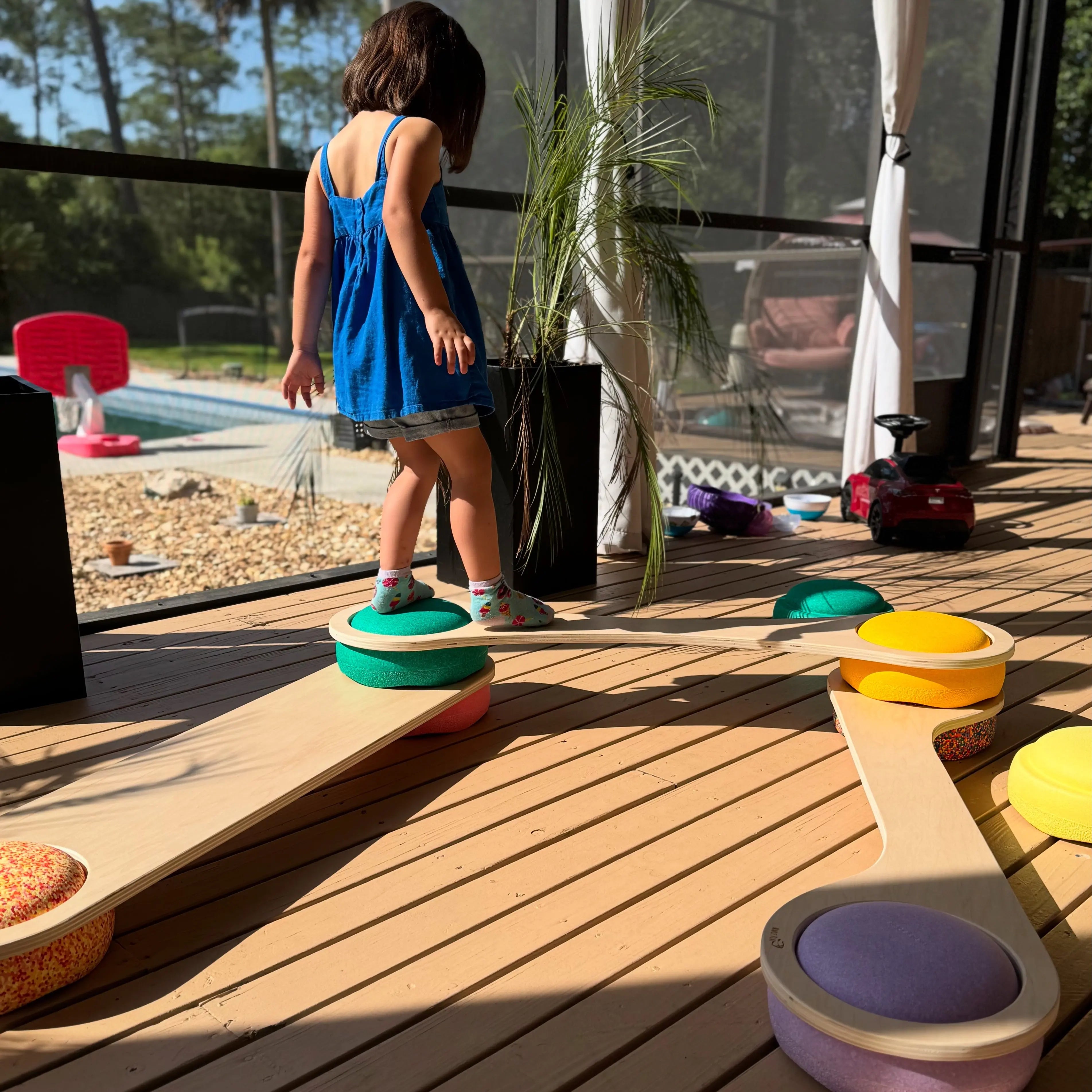 Child playing on wooden balance board with colorful cushions outdoors.
