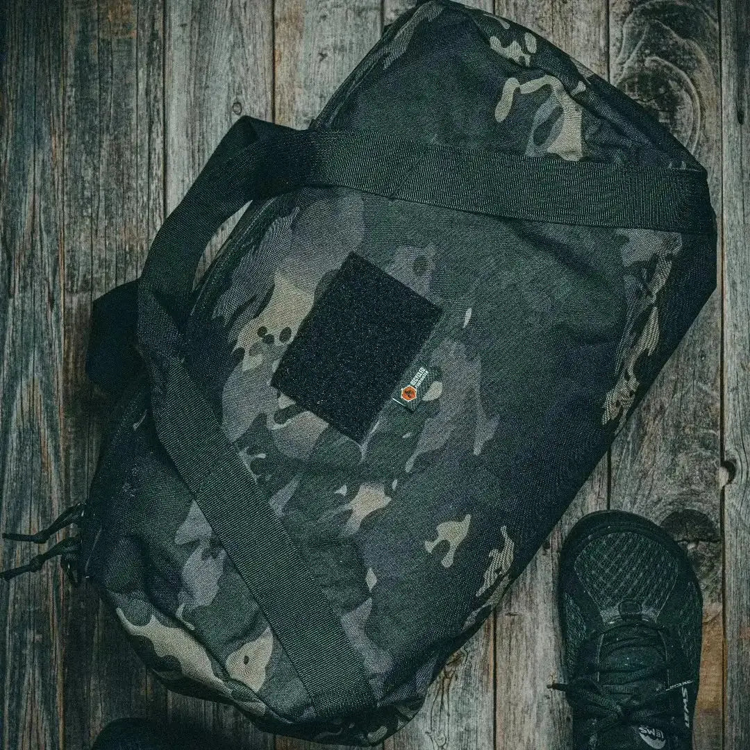 Camouflage barrel duffle bag on a wooden background with a black shoe.