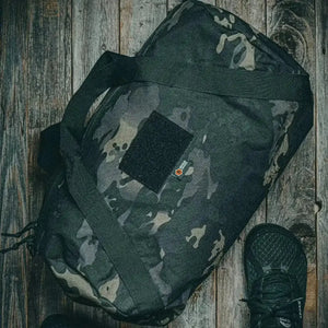 Camouflage barrel duffle bag on a wooden background with a black shoe.